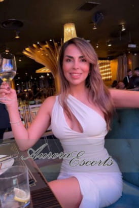 A sexy Chilean girl sitting at a table holding a glass of wine