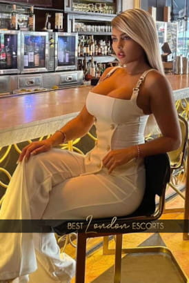 Beautifully turned out busty Colombian girl sitting at a table in a bar