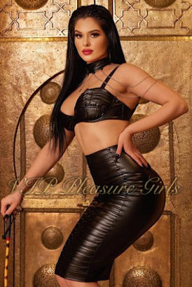 Tall, dark haired Mistress in PVC skirt and bra with a leather choker