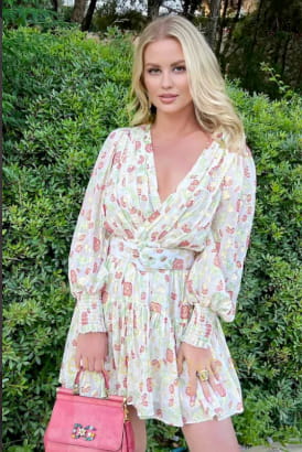 Beautiful blonde girl in a flowery summer dress and holding a chic pink clutch bag